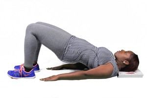 A woman in a gym, doing yoga or stretching exercises with her hands on the floor and her body extended.