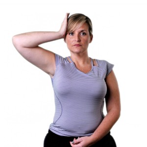 A woman wearing a striped tank top, with her hand on her head and her elbow extended, in front of a white background.