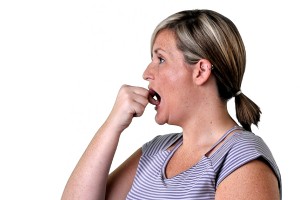 A woman with blonde hair, wearing a striped shirt and ponytail holder, is holding her hand to her mouth in a surprised or shocked manner.