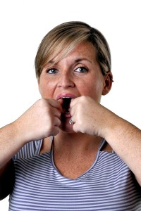 A woman with blonde hair, wearing a striped top, holding her hand to her mouth.