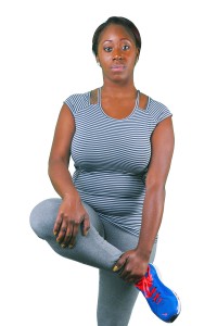 Woman in black and white striped tank top, blue sneakers, and gray leggings posing with one hand on hip and the other on thigh.