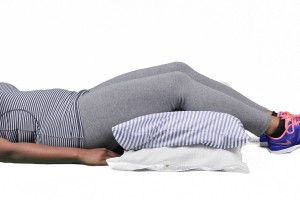 The image shows a person lying on their back with one leg raised, wearing a sports bra and leggings, with a gym bag nearby.