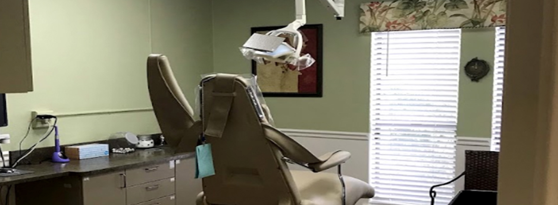 The image depicts a dental office interior, featuring a dental chair and a desk with a computer monitor.