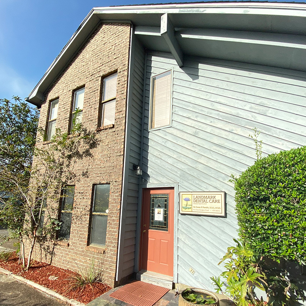 The image shows a two-story building with a prominent sign that reads  Lighthouse Christian Church.  It has a brick facade and is topped by a white roof. The entrance features a red door and a small porch area. In front of the building, there are plants and a sidewalk leading up to the entrance.